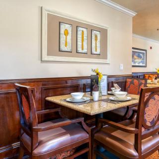 A cozy dining area in a restaurant with a table set for two, featuring elegant wooden chairs and framed wall art.