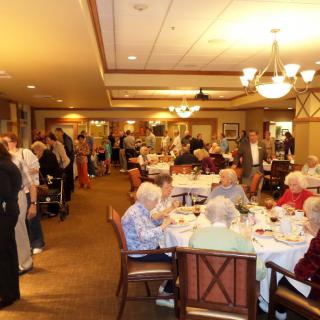A group of elderly people enjoying a meal together in a dining hall setting.