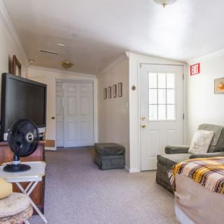 A cozy living room with a TV, couch, and fan, featuring a door leading to another area.