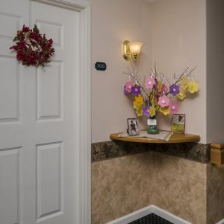 A hallway with a decorated door, floral arrangement, and wall sconce lighting.