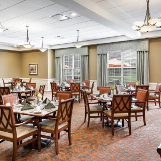 A well-lit dining room with neatly arranged tables and chairs, featuring elegant decor and large windows.