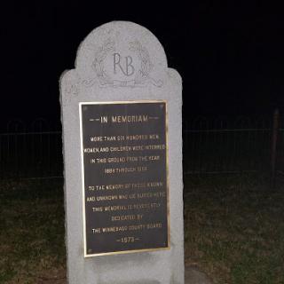 A memorial stone with a plaque, illuminated at night.