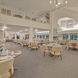 A spacious dining room with neatly arranged tables and chairs under bright lighting and a prominent chandelier.