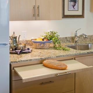 A cozy kitchen setup featuring a pull-out cutting board with a loaf of bread, surrounded by kitchen decor and a granite countertop.