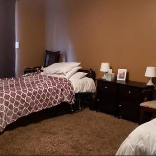 A cozy bedroom featuring two beds with patterned bedspreads, carpet flooring, and nightstands with lamps.