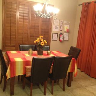 A cozy dining room featuring a table with a colorful tablecloth, surrounded by chairs and decorated with a vase of sunflowers under a chandelier.