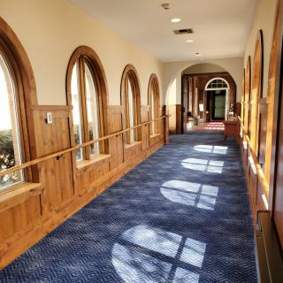 A sunlit hallway with arched windows and a blue carpet.