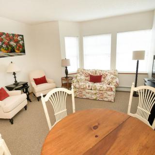 A cozy living room with floral and neutral tones, featuring a sofa, armchairs, and round wooden table.