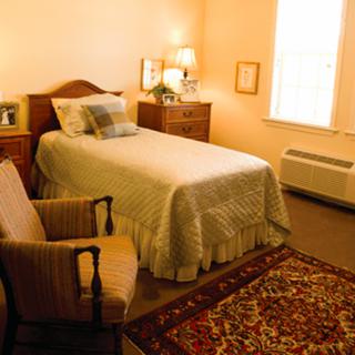 A cozy bedroom with a single bed, armchair, and warm lighting.