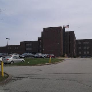 A view of a brick hospital building with an adjacent parking lot and flags flying.