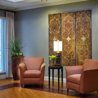 A cozy living room setup featuring two brown chairs, decorative artwork on the wall, a lamp, and a touch of greenery.