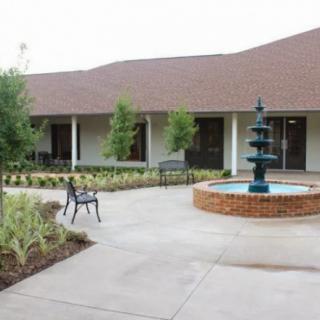 A peaceful courtyard featuring a fountain, surrounded by greenery and a bench.
