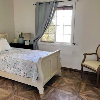 A cozy bedroom featuring a single bed, a window with curtains, and an elegant chair.