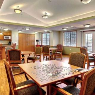 A well-lit dining area with wooden tables and chairs, featuring a partially completed puzzle on one of the tables.
