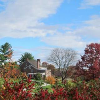 A scenic view of a house surrounded by colorful autumn foliage under a partly cloudy sky.