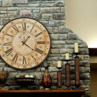 A rustic stone wall with a large clock and candles on a mantel.