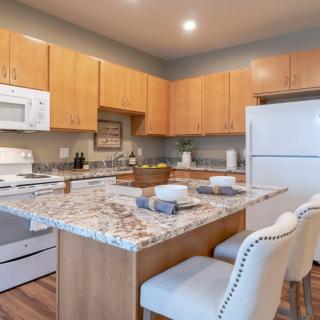 A modern kitchen with granite countertops, wood cabinets, and white appliances.