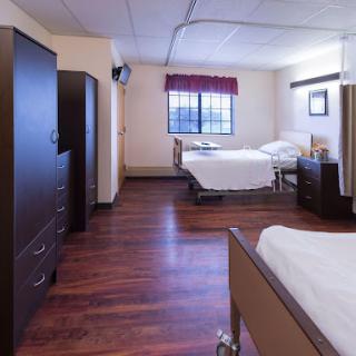 A well-lit hospital patient room featuring two beds and essential furniture.