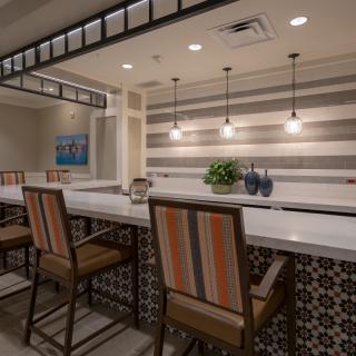 A modern bar interior featuring a sleek counter with high-backed chairs, pendant lighting, and a striped accent wall.