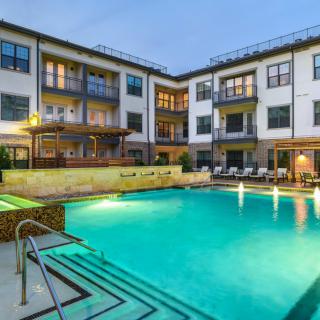 Modern apartment complex with a lit outdoor swimming pool in the evening.