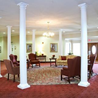 A spacious living room with classic furniture, a central rug, and prominent columns.