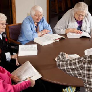 A group of elderly individuals sitting around a table, each engaged in reading books.