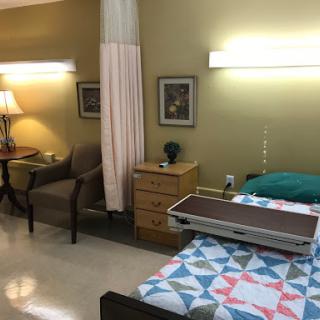 A well-organized hospital patient room featuring a bed, seating area, and soft lighting.