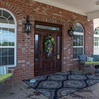A welcoming front porch with a brick exterior, featuring a decorative wreath on the door, lantern-style lights, and comfortable outdoor seating.
