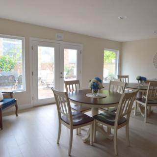 A bright dining room with a glass table and chairs, illuminated by natural light from large windows.
