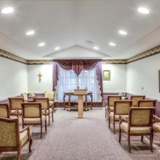 A small chapel interior with rows of chairs facing an altar, illuminated by ceiling lights.