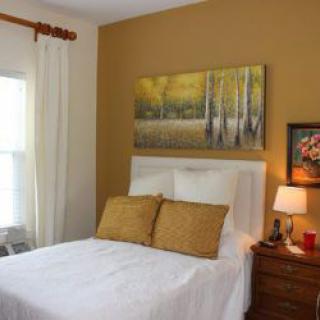 A cozy bedroom interior with a bed, decorative pillows, artwork on the walls, and a bedside lamp.