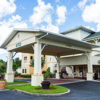 The image shows the exterior entrance of a building with a covered driveway and landscaped surroundings.