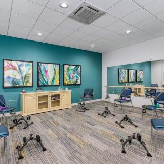 A modern exercise room equipped with chairs and colorful paintings, featuring mirrors and stylish decor.