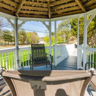 A tranquil gazebo with chairs overlooking a sunny garden.
