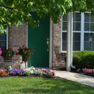A charming brick house with a green door, surrounded by a well-maintained garden and colorful flowers.
