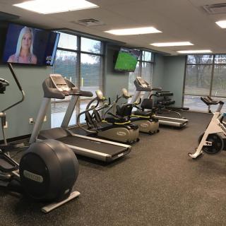 A modern gym featuring treadmills, elliptical machines, and exercise bikes with TV screens.