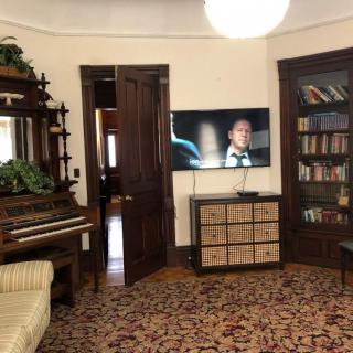 A cozy living room with vintage furniture, featuring a piano, a bookshelf, and a television.