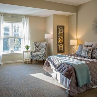 A cozy bedroom with natural light streaming through a large window, featuring elegant decor and a comfortable bed.