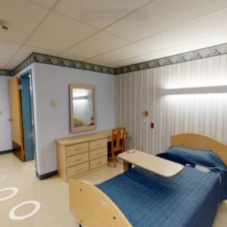 A hospital room with a bed, dresser, and mirror in a medical facility.