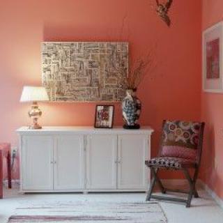 A stylish living room with coral walls features a white sideboard, artistic decor, and a patterned chair.