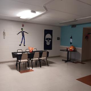 A festive Halloween-themed room decorated with skeletons, pumpkins, and wall art, ready for a gathering.
