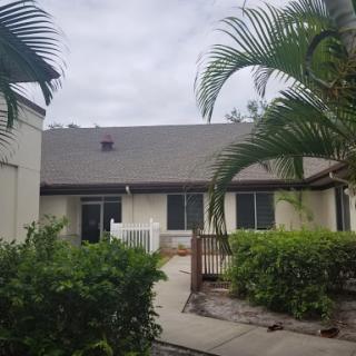 A cozy residential building surrounded by lush greenery and palm trees under a cloudy sky.