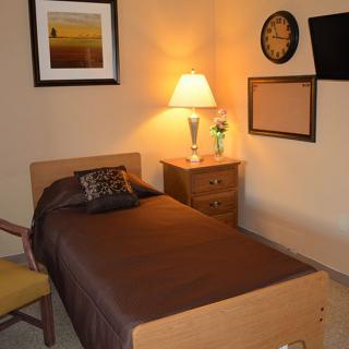 A cozy bedroom with a single bed, nightstand, lamp, chair, and wall decorations.