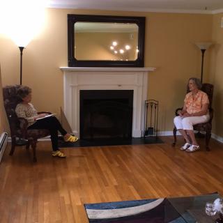 Two people sitting in a living room with a fireplace, engaging in conversation.