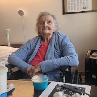 An elderly woman sitting in a wheelchair, enjoying a moment indoors with food.