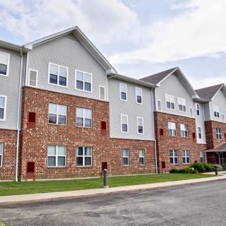 A three-story residential apartment building with a brick facade and multiple windows under a cloudy sky.