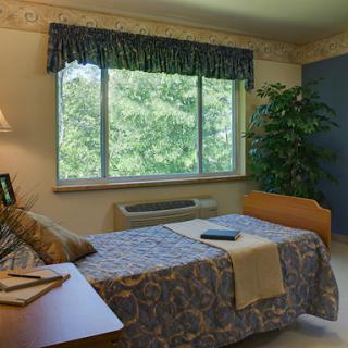 A cozy bedroom featuring a large window with a view, neatly made bed, and decorative touches.
