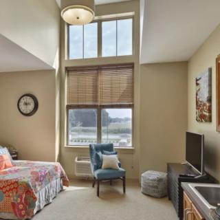 A cozy bedroom with a large window, featuring a bed, chair, and television.