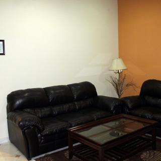A cozy living room with black leather sofas, a glass-top coffee table, and a floor lamp against an orange accent wall.