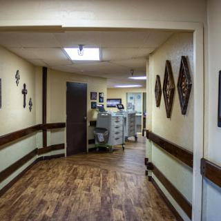 A view of a well-lit hallway in a healthcare facility, featuring wooden flooring and decorative elements on the walls.